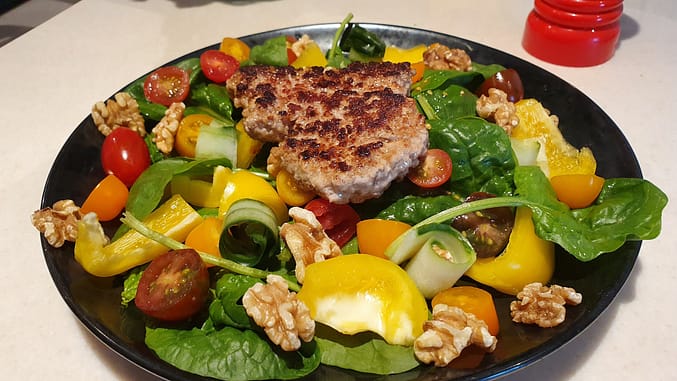 A healthy plate example - organic spinach salad with small tomatoes, cucumber, pepper, walnuts, olive oil and lemon, together with organic pork.